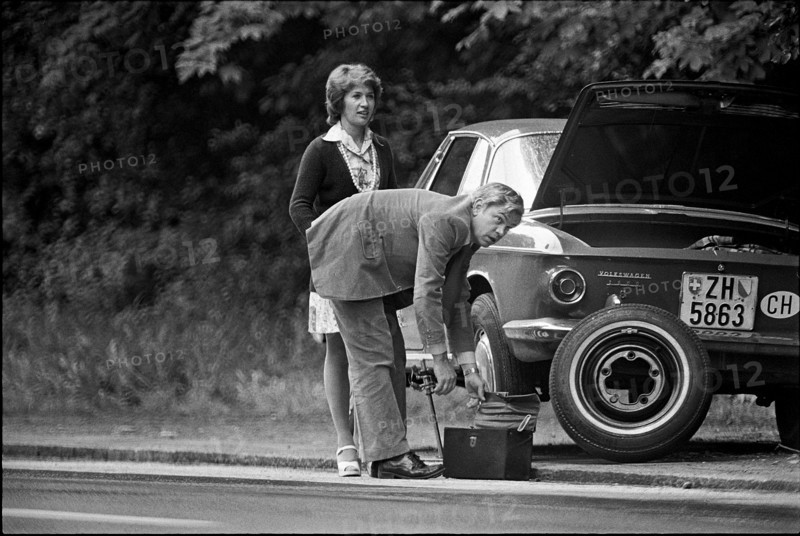 Man helping woman driver after puncture, 1974