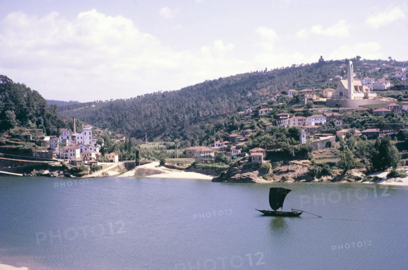 A series of images about port wine production in Portugal c 1960 - traditional rabelo boat sailing boat passing River Douro village.