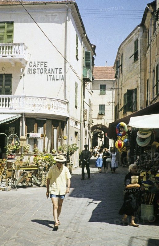 People walking along street, Laigueglia, Savona, Italy, July 1959.