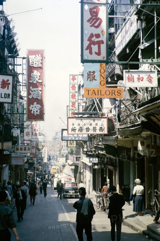 Busy street of shops and signs in English and Mandarin including for Tai Cheong Tailors, Wellington Street, Hong Kong, Asia 1964.
