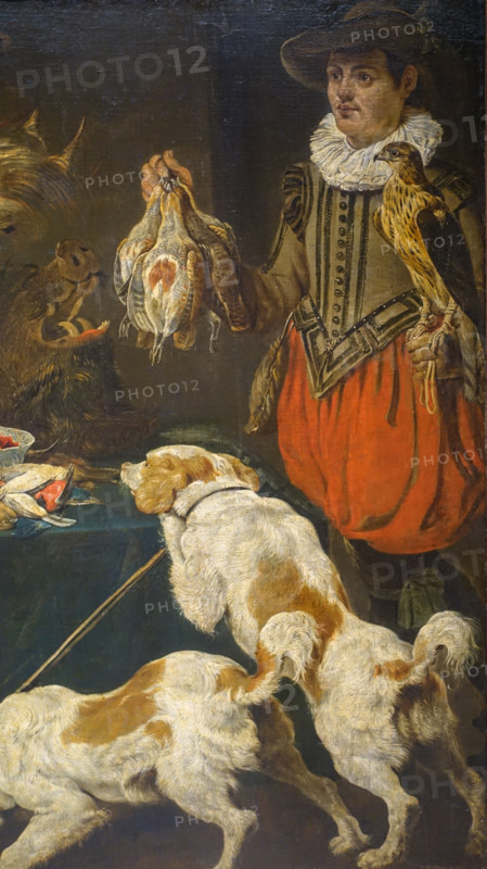 Hunter with dogs at a table with poultry and fruit.