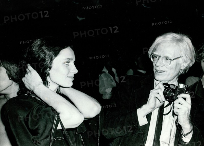 Andy Warhol holds a camera as Margaret Trudeau pulls back her hair
