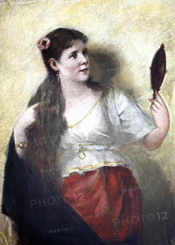 At her toilet, a young woman with long hair looks into a hand mirror, 1895