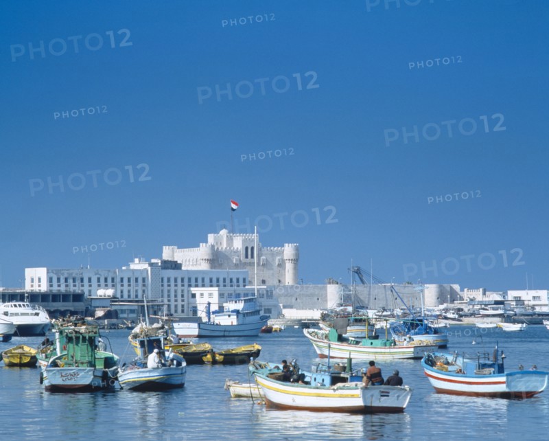 EGYPT, Nile Delta, Alexandria, Fishing boats moored in harbour with fortress castle and walls beyond.