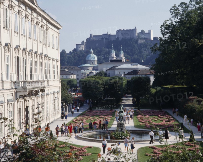 AUSTRIA, Salzburg Province, Salzburg, Mirabell Palace with tourists walking in the formal gardens with Hohensalzburg Fortress on the overlooking hill