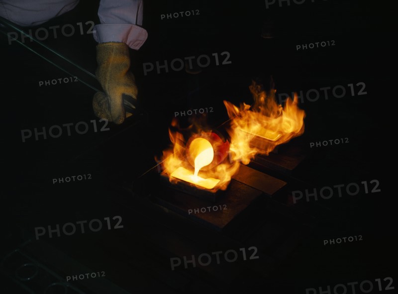 INDUSTRY, Factory, Gold Manufacturing, Gloved hand holding pole pouring molten gold into flaming mould