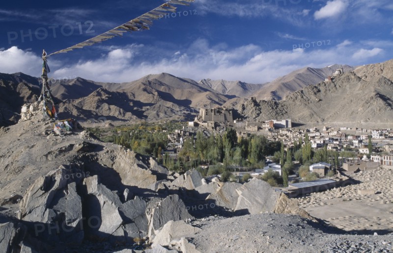 INDIA, Ladakh, Leh, Prayer flags blowing in the wind on top of rocks in the foreground overlooking town surrounded by mountains