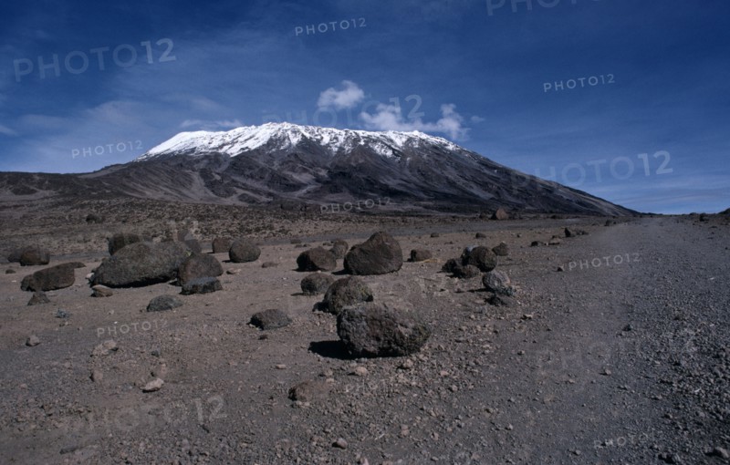 TANZANIA, Kilimanjaro, Snow capped Mount Kilimanjaro with large boulders of rock in the foreground