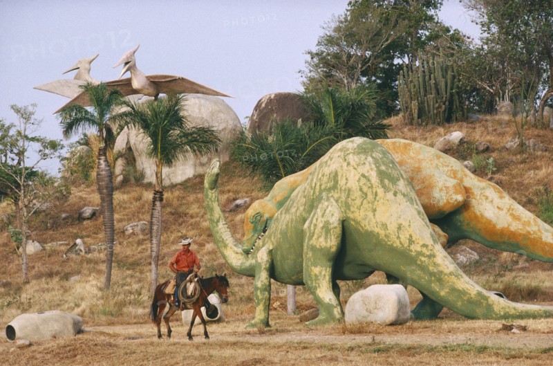 CUBA, Santiago De Cuba, Buccanao, Parco Prehistorico dinosaur replicas with man on horseback riding past