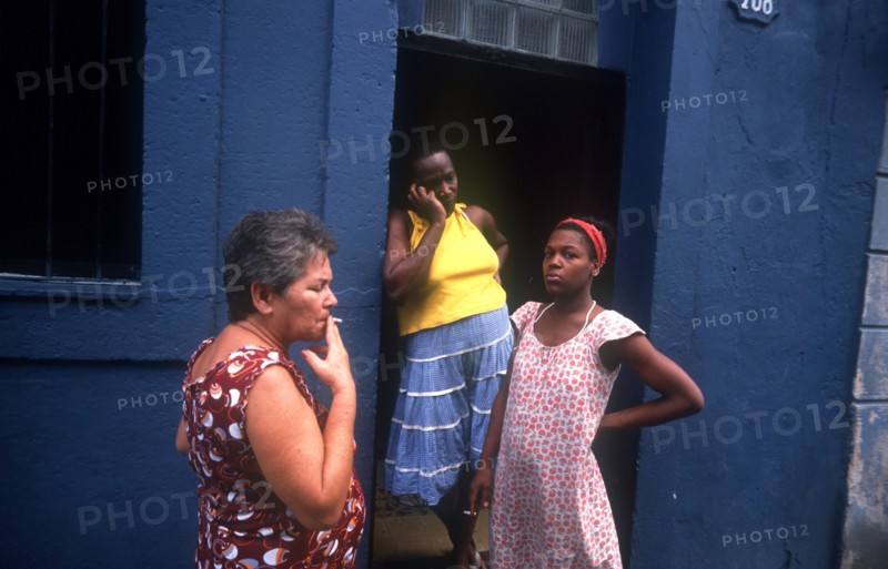 CUBA, Havana, Three women gathered by a doorway of a blue house smoking