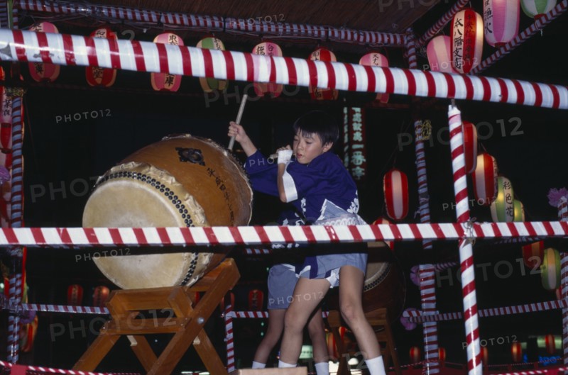 JAPAN, Honshu, Tokyo, Young boy in costume beating a large drum at the O-Bon festival