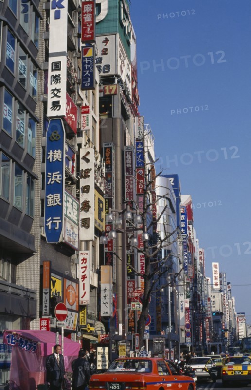 JAPAN, Honshu, Tokyo, Advertising down the side of buildings in the Shinjuku district with the street busy with traffic and pedestrians