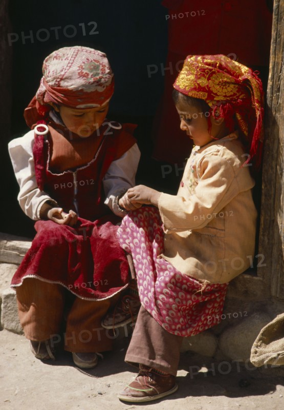 CHINA, Xinjiang Province, Children, Two Tadjik girls sitting on step beside wooden door frame.