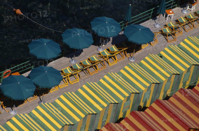 ITALY, Campania, Sorrento, "View over green and yellow and red and yellow striped beach huts, green and yellow striped deck chairs and green sun umbrellas on wooden decking."