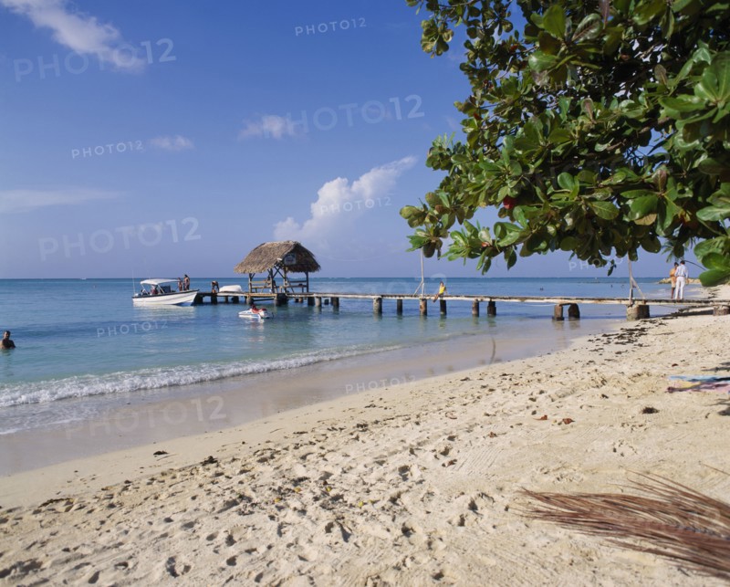 WEST INDIES, Tobago, Pigeon Point, Sandy beach with boats at wooden jetty with tree leaves from right and foot prints in sand