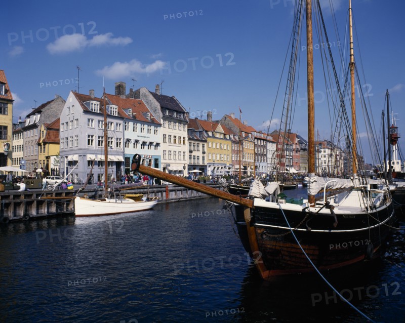 DENMARK, Zealand, Copenhagen, Nyhavn harbour. Traditional waterfront buildings with moored boats and a schooner in the foreground