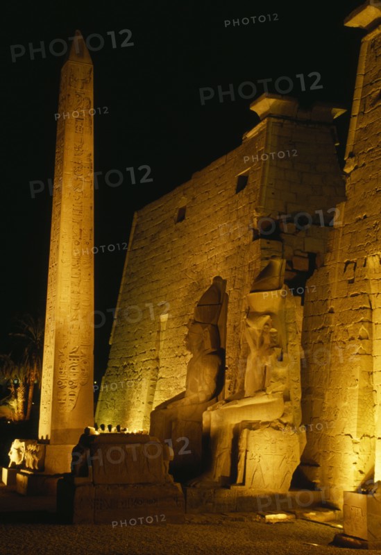 EGYPT, Luxor, The temple illuminated at night seated statues of Ramesses II outside the Pylon with the Obelisk