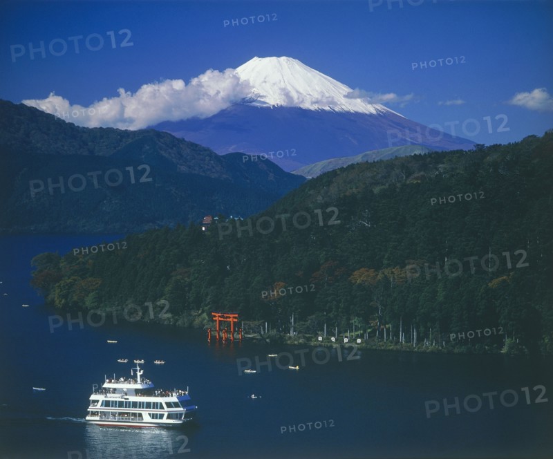 JAPAN, Honshu, Ashino Lake, Mount Fuji with snow cap above the lake with a passenger boat passing the Hakone torii gate