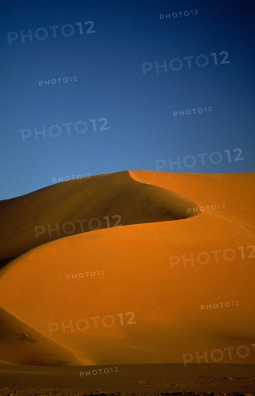 LIBYA , South West, Achan , Orange desert sand dune against a clear blue sky