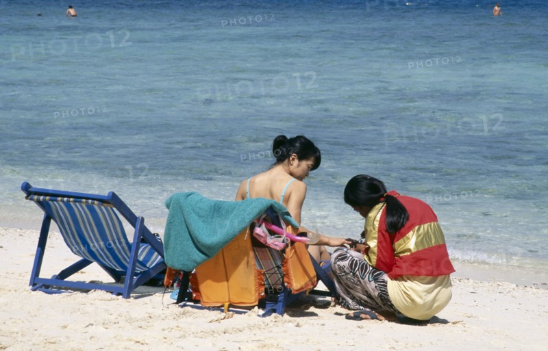 THAILAND, Phuket, Koh Hi, Also known as Coral Island. Japanese tourist sitting in a deck chair on the beach having a manicure