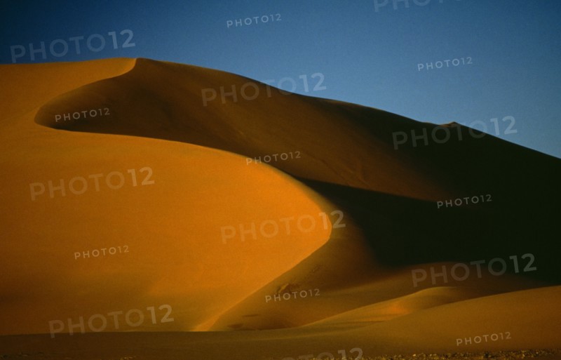 LIBYA , Achan, Sand dune partially cast in shadow against blue sky