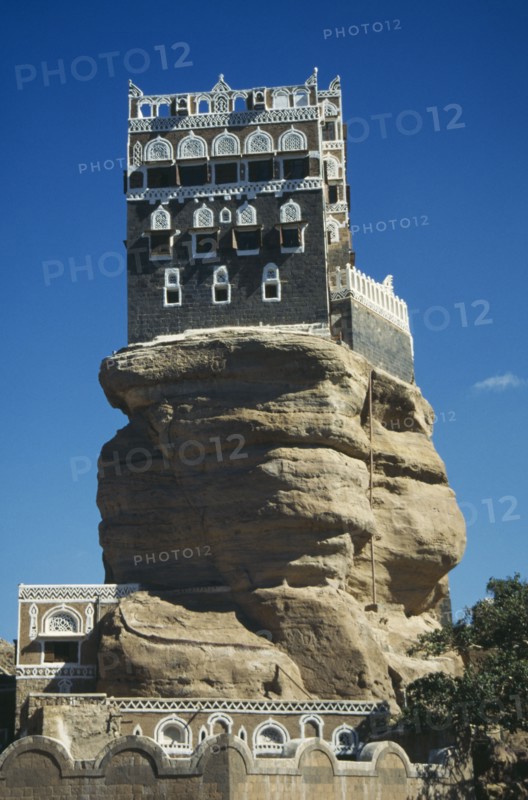 YEMEN, Wadi Dhar, Palace of the Rock, View looking up at grey and white building perched on top of  rock.