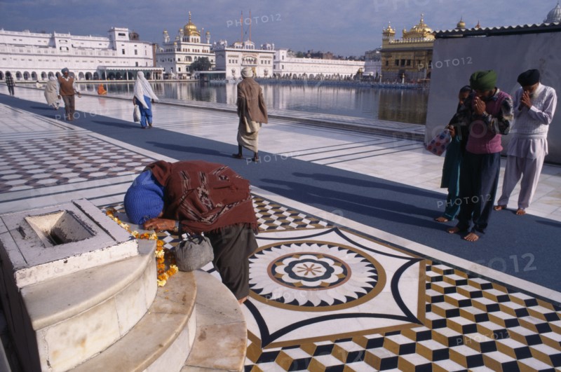 INDIA, Punjab, Amritsar, Barefooted pilgrims saying prayers at Golden Temple complex with offering of marigold flower garland lying on marble step.