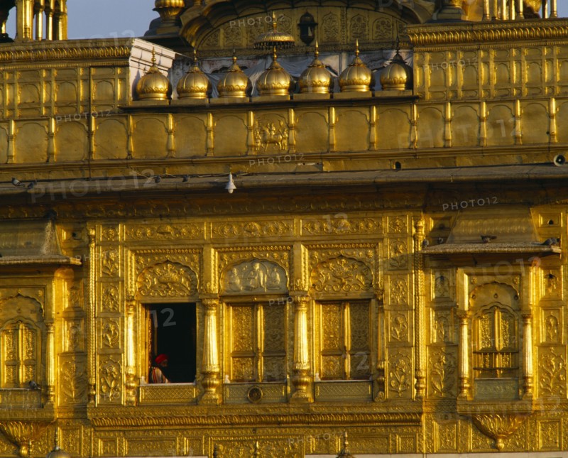 INDIA, Punjab, Amritsar, The Golden Temple.  Detail of golden exterior wall with man framed in window.