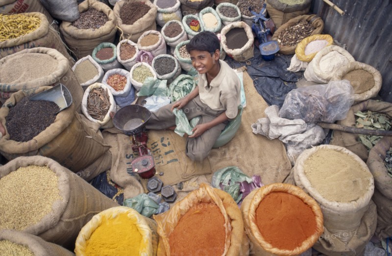 INDIA, Delhi , Spice market, View looking down on young vendor sitting at scales in the middle of sacks of spices