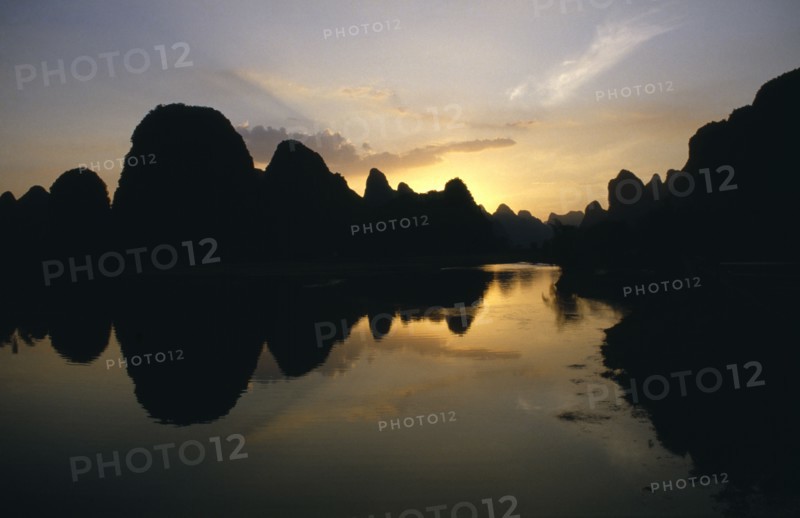 CHINA, Guangxi, Guilin , View over River Li lined with towering rock fromations silhouetted at sunset