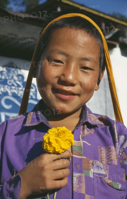 INDIA, Sikkim, Tashiding, Smiling boy holding yellow marigold.