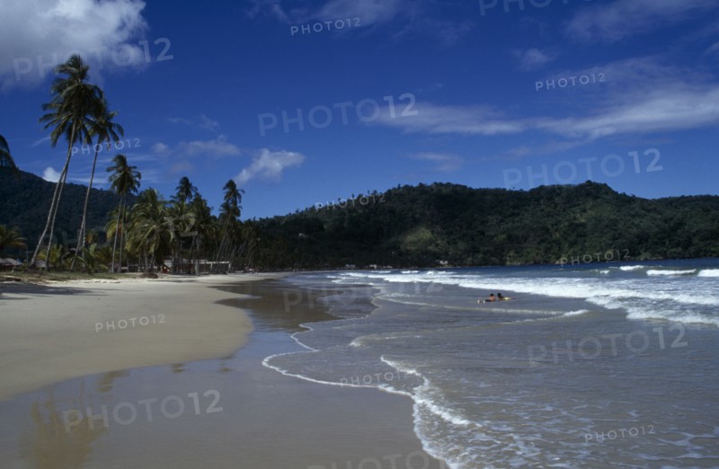 WEST INDIES  , Trinidad, Maracas Bay , Sandy beach with couple lying in the surf and tree covered headland beyond.
