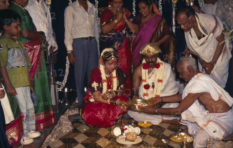 INDIA, Bangalore , Hindu Wedding, People standing around sitting couple wearing traditional wedding dress.