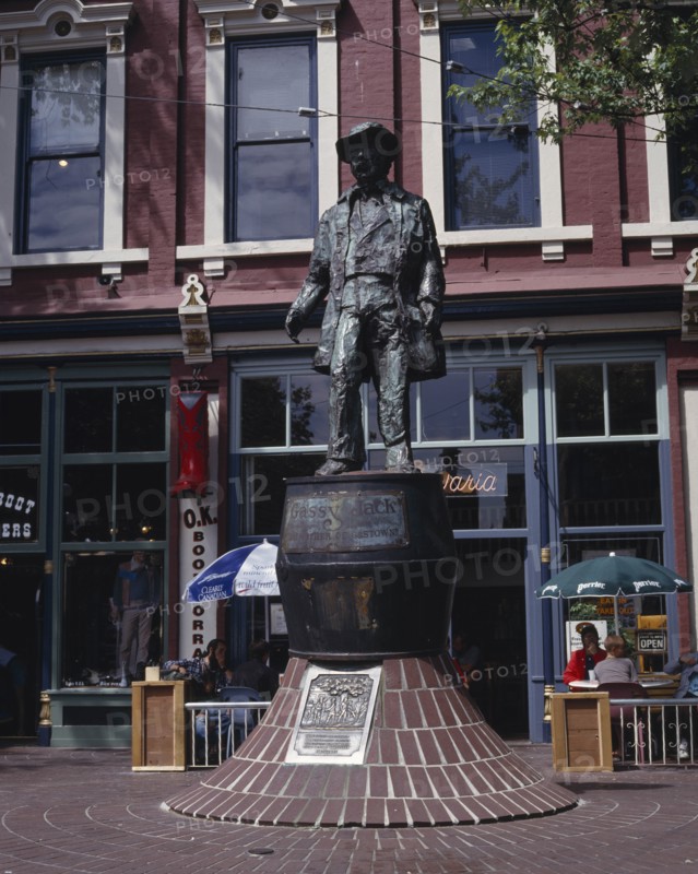 CANADA, British Columbia, Vancouver, Gastown. Bronze statue of Gassy Jack the father of Gastown with a cafe behind