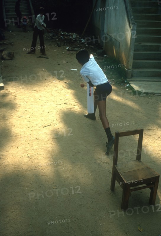 SRI LANKA, Kandy, Young boys playing Cricket in street using a wooden chair as stumps