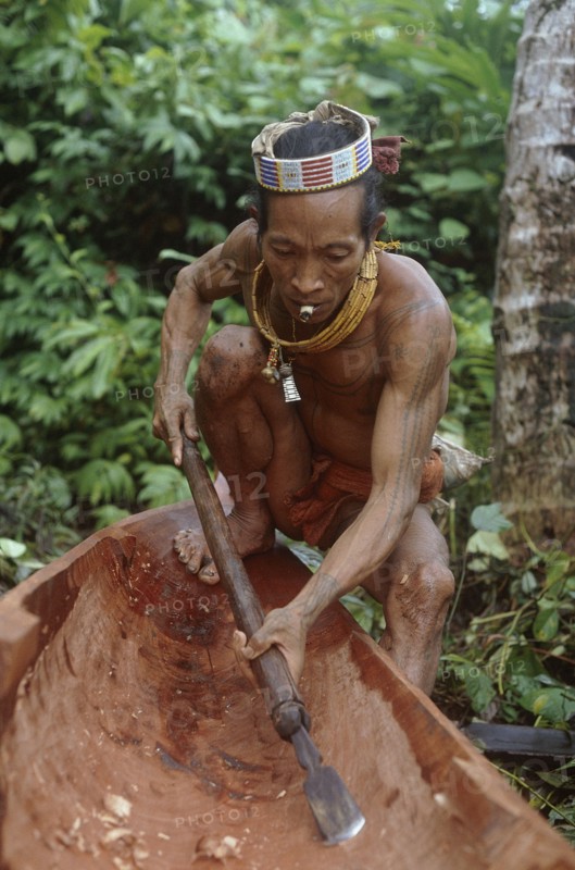 INDONESIA, Sumatra, Siberut Island, A Mentawi man hollowing out a canoe whilst he smokes a hand rolled cigarette
