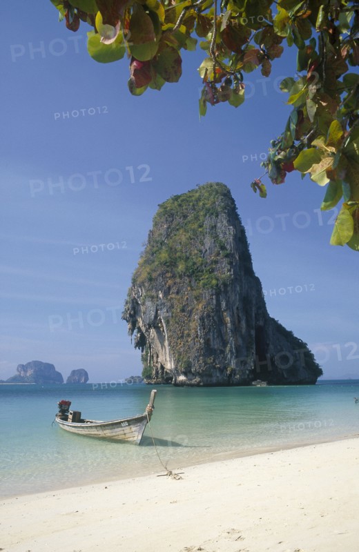 THAILAND, Krabi Province, Phra Nang Beach, Long tail boat in clear calm blue water at the edge of he beach with limestone islands behind