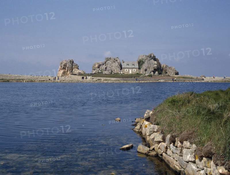 FRANCE, Brittany , Plougrescant, Overlooking an expanse of water to a house surrounded by rocks.