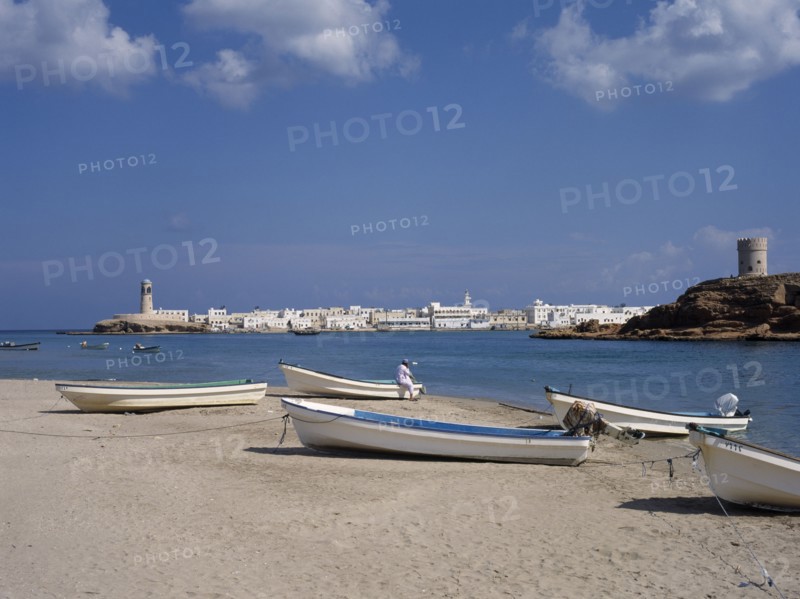 OMAN, Sur , Harbour with boats pulled up on stretch of sand with town and hilltop tower behind.