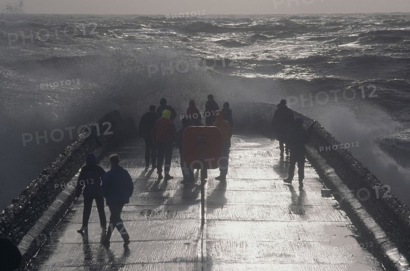 ENGLAND, East Sussex, Brighton, Waves crashing over a groyne with people on it