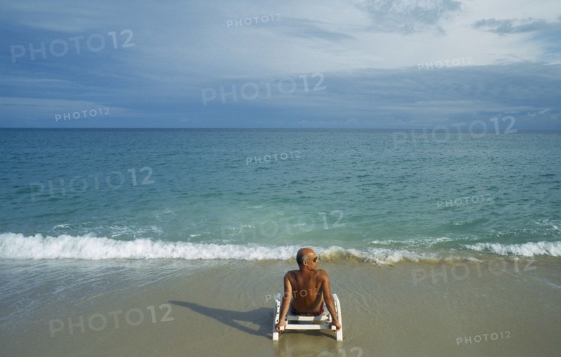 THAILAND, Surat Thani, Koh Samui, Lamai beach with lone male tourist sitting on a sunbed on the empty beach