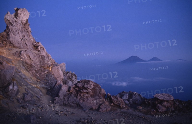 INDONESIA, Java, Mount Merapi, View from the rocky summit of the volcano with peaks in the distance above misty blue blanket of cloud