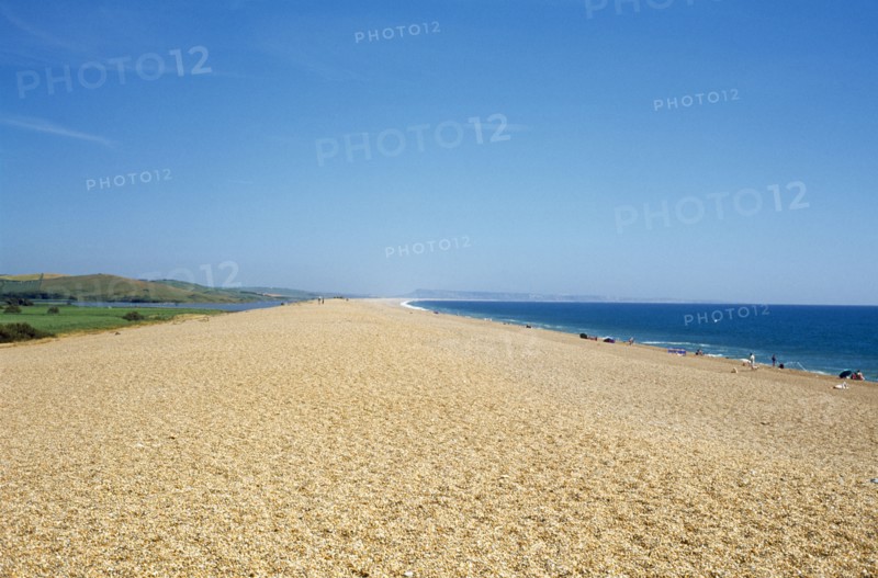 ENGLAND, Dorset, Chesil Beach, The shingle beach and lagoon stretching towards distant horizon with sunbathers along the shoreline.