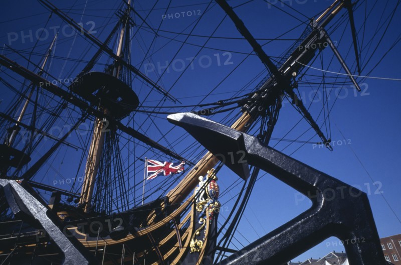 ENGLAND, Hampshire, Portsmouth, Admiral Lord Nelson’s HMS Victory in Portsmouth’s Historic Dockyard.  Angled view of bow of ship with figurehead and Union Jack flag.  Anchor in foreground.