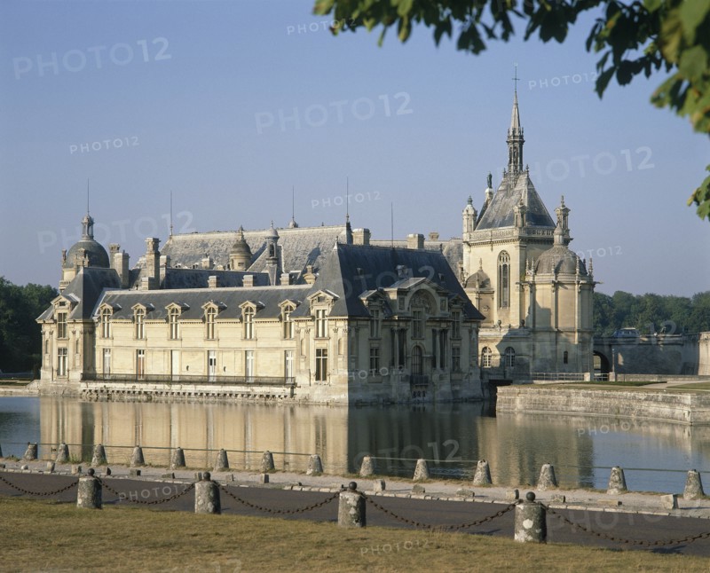 FRANCE, Nord Picardy, Oise, Chantilly Chateau with its reflection in surrounding water and a road in the foreground
