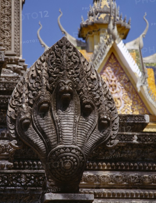 CAMBODIA, Phnom Penh, Stone carving of naga on temple stupa with roof of Silver Pagoda part seen behind.