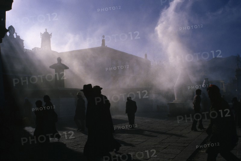 10122739 TIBET   Lhasa Jokhung Square.  People silhouetted in sunlight through smoke.