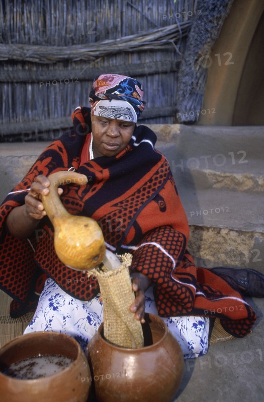 SOUTH AFRICA, Qwa Qwa, Basotho Cultural Village, Basotho woman pouring beer into a strainer from a gourd