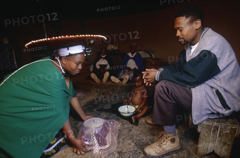 SOUTH AFRICA, Kwa Zulu Natal , Msinga, Zulu woman kneeling to give tea to her seated husband.