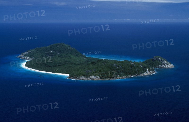 SEYCHELLES, North Island, Aerial, View over whole Island with white sand beach and interior covered by dense vegetation.  Deep blue sea.